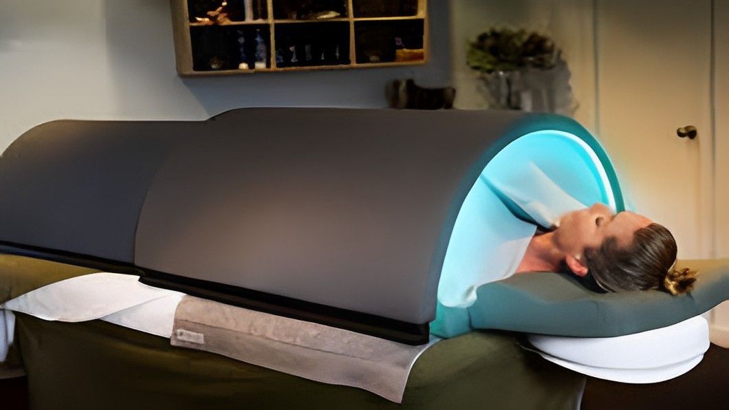 A woman is laying in a sauna with a blue light coming out of it.