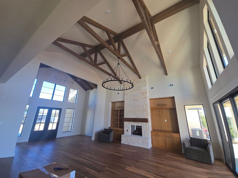 Spacious living room with vaulted ceilings, wooden beams, a stone fireplace, large windows, and dark wood flooring.