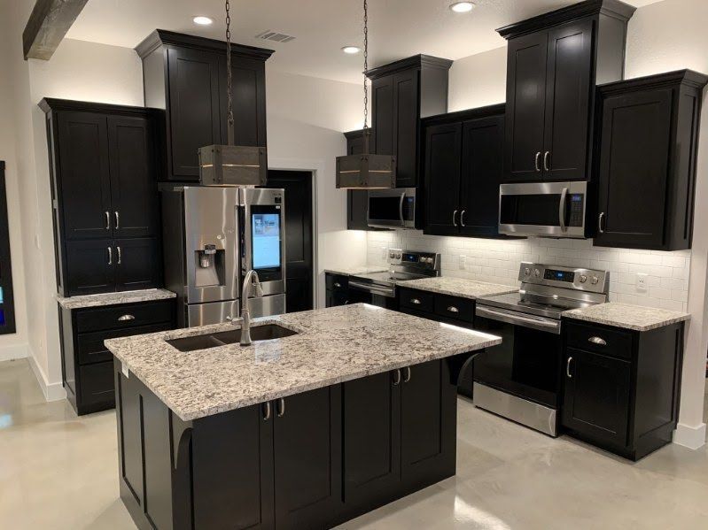 Modern kitchen with dark cabinets, granite island, stainless steel appliances, and white backsplash.