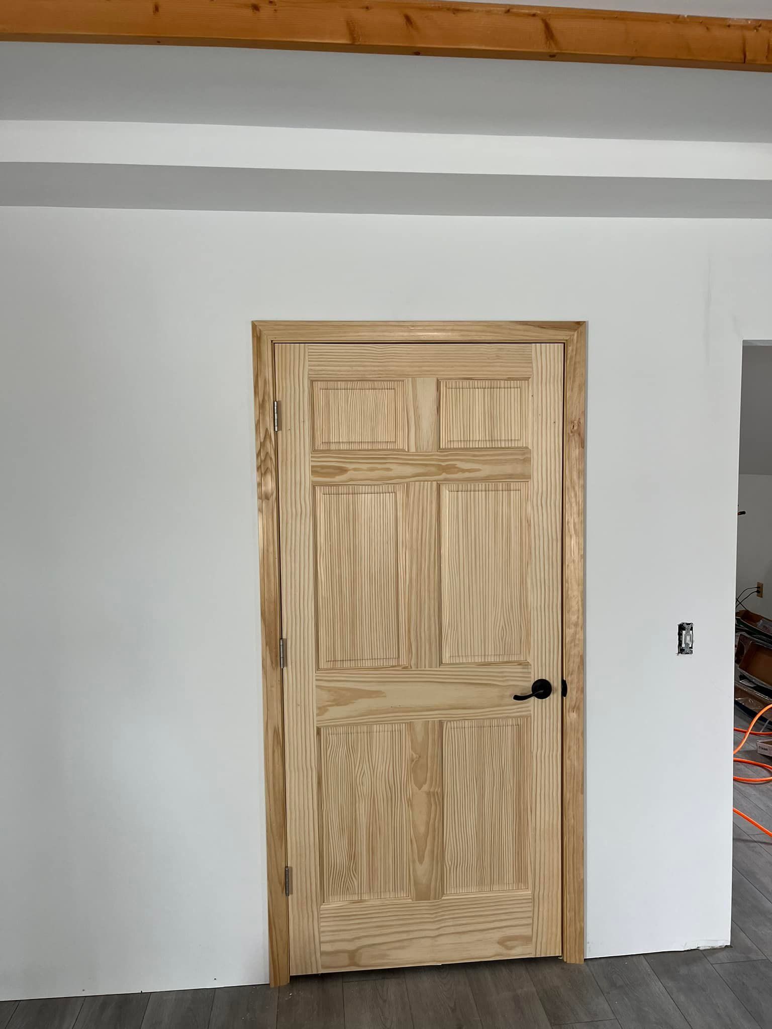 Wooden interior door with a black handle set in a white wall.
