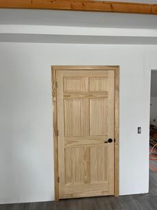 Wooden interior door with a black handle set in a white wall.