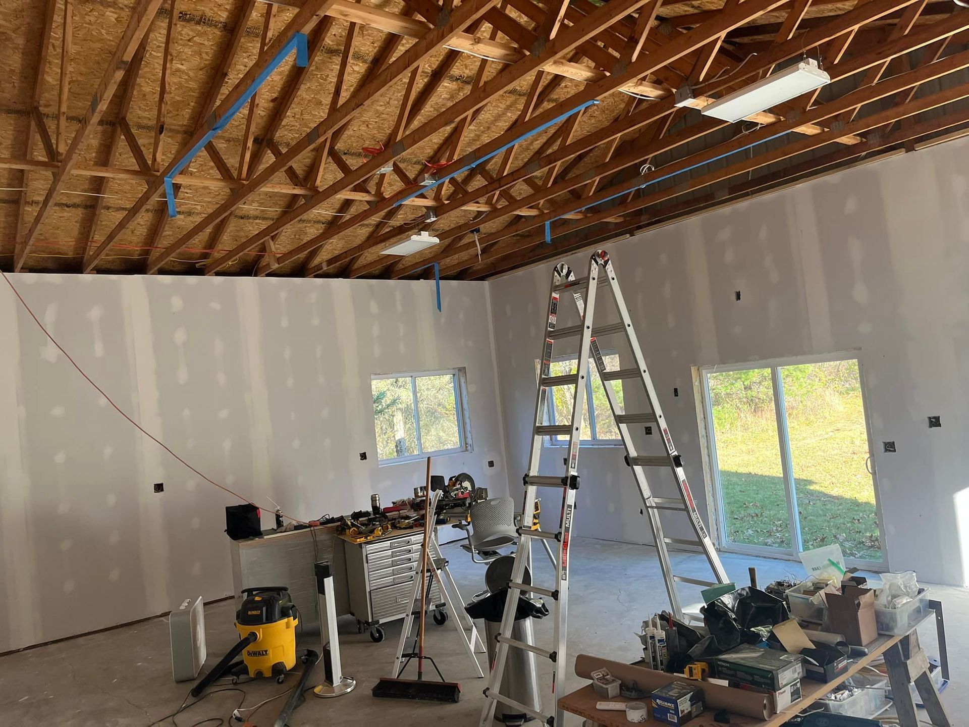 Interior view of a room under construction, drywall installed. A ladder and tools are present.