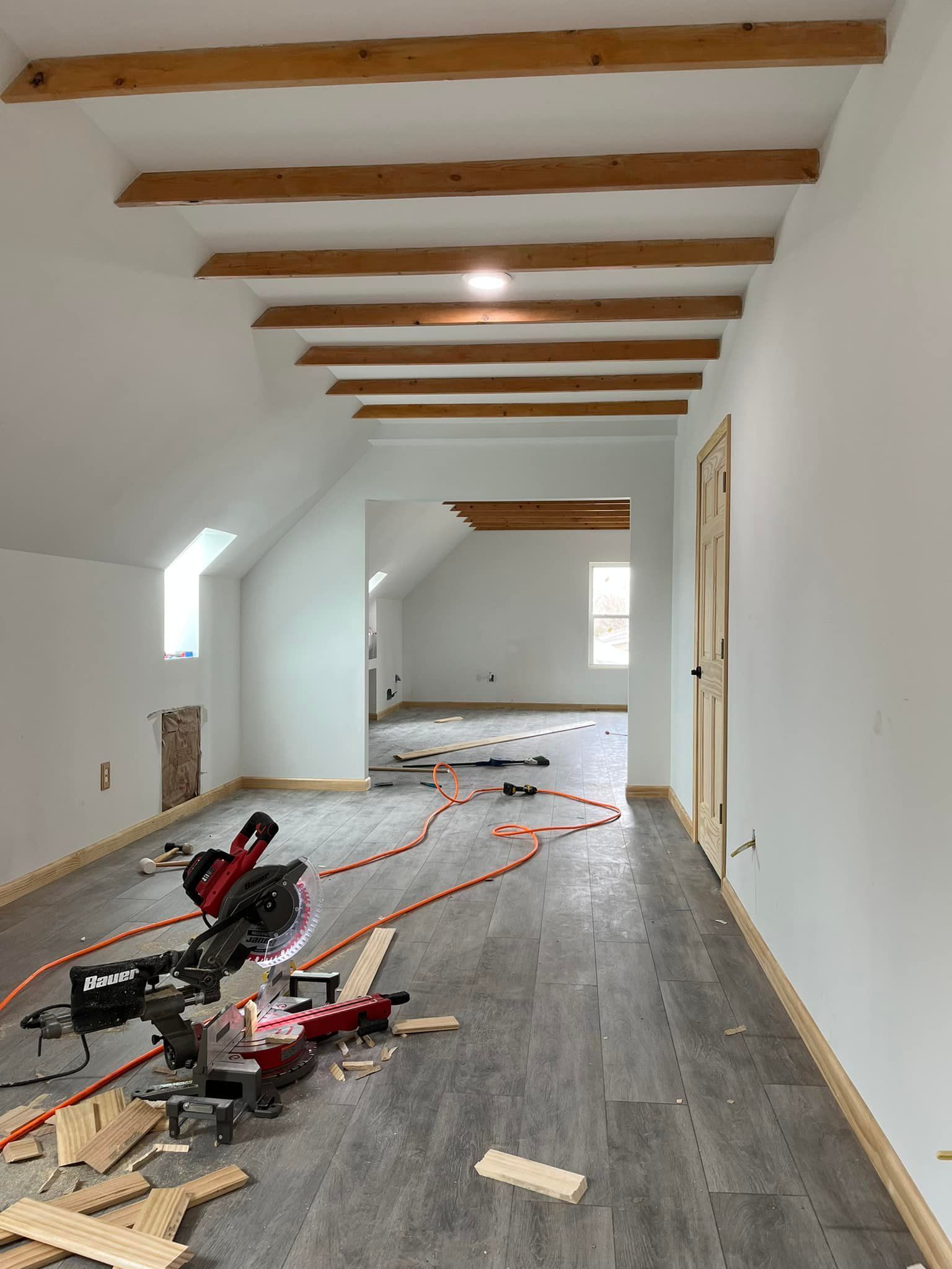 Interior view of a construction site with a saw, exposed beams, and gray flooring.