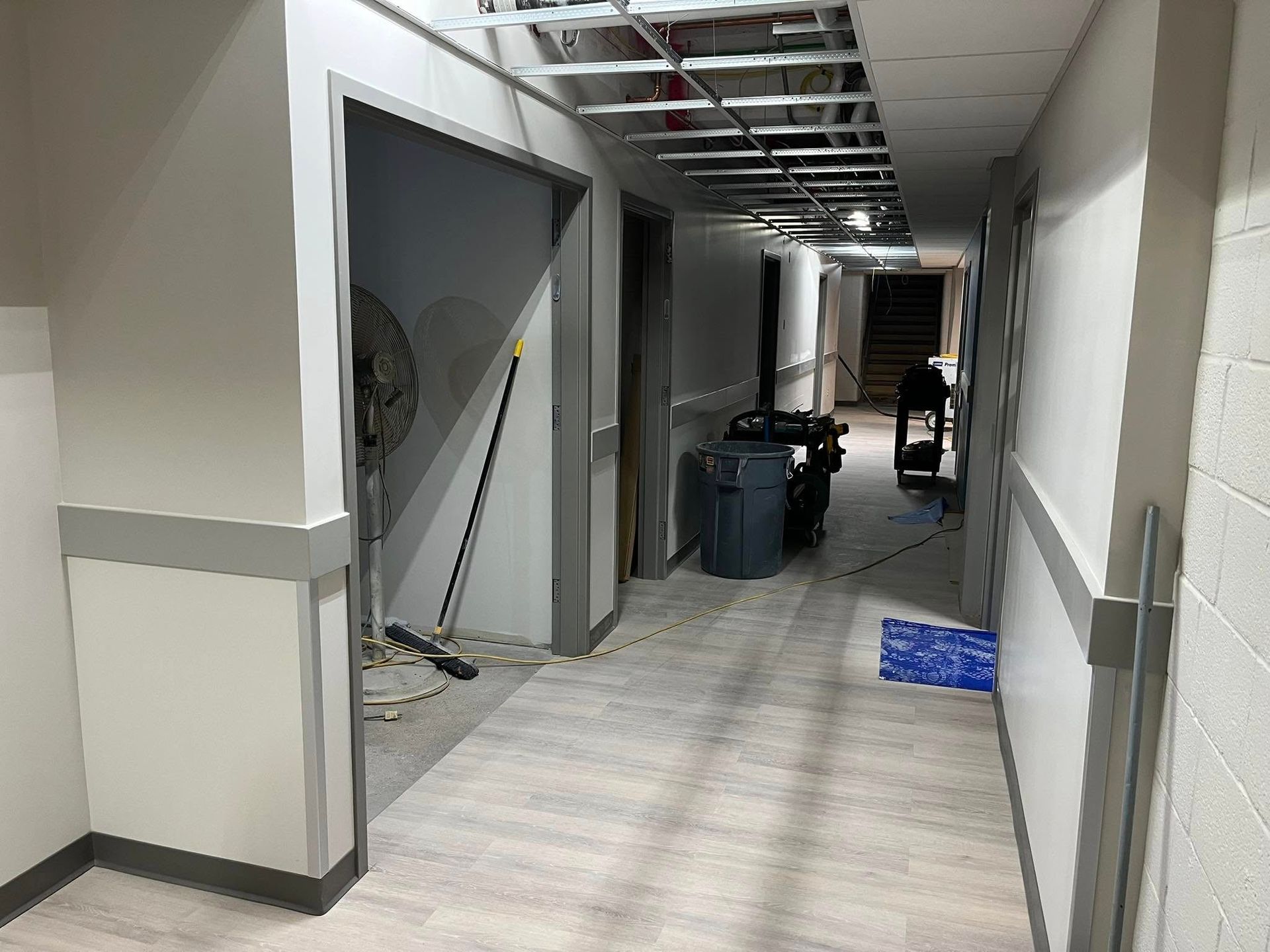 Hallway under construction with exposed ceiling, open doorways, and cleaning equipment.