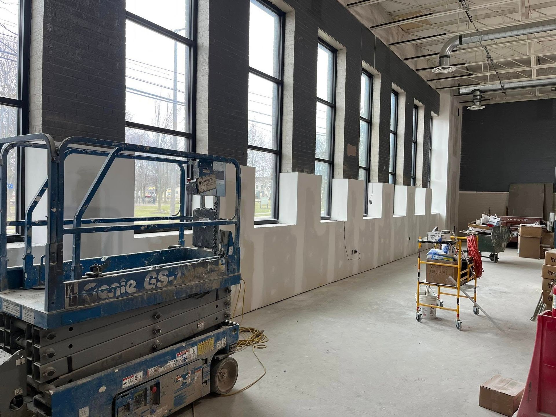Construction site with a scissor lift near a wall with windows; unfinished drywall.