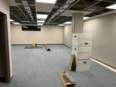 Room under construction with exposed ceiling, blue carpet, boxes, and tools.