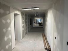 Long hallway under construction with drywall, exposed ceiling, and construction materials.