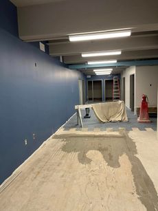 Interior hallway under construction; blue wall, gray ceiling beams, concrete floor.