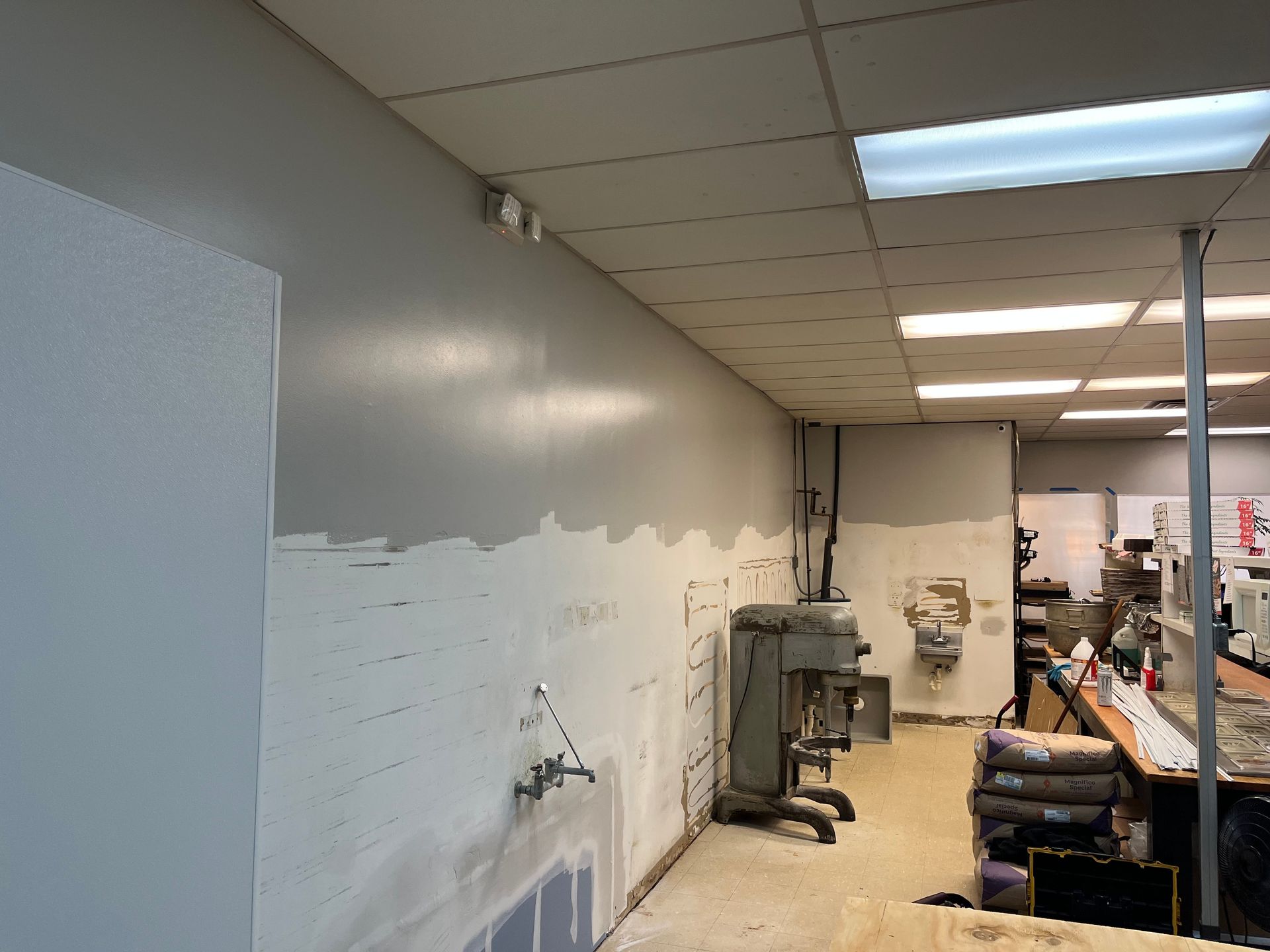 Interior of a room under construction. Gray walls, unfinished paint, exposed fixtures, and industrial equipment.