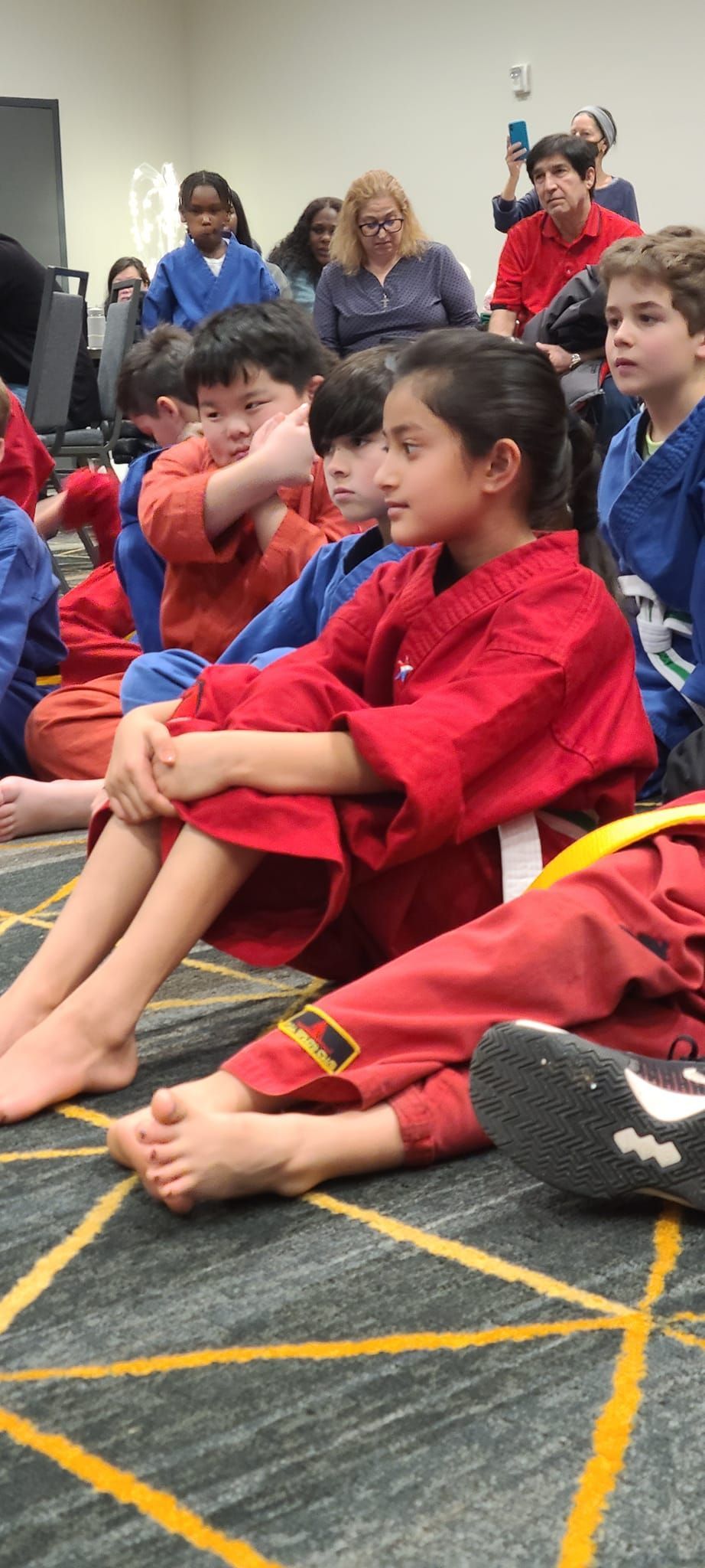 a group of children in karate uniforms are sitting on the floor .