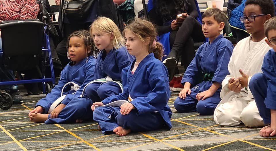a group of young children in blue karate uniforms are sitting on the floor .