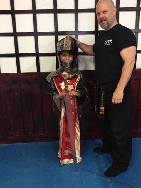 a man is standing next to a young boy in a knight costume