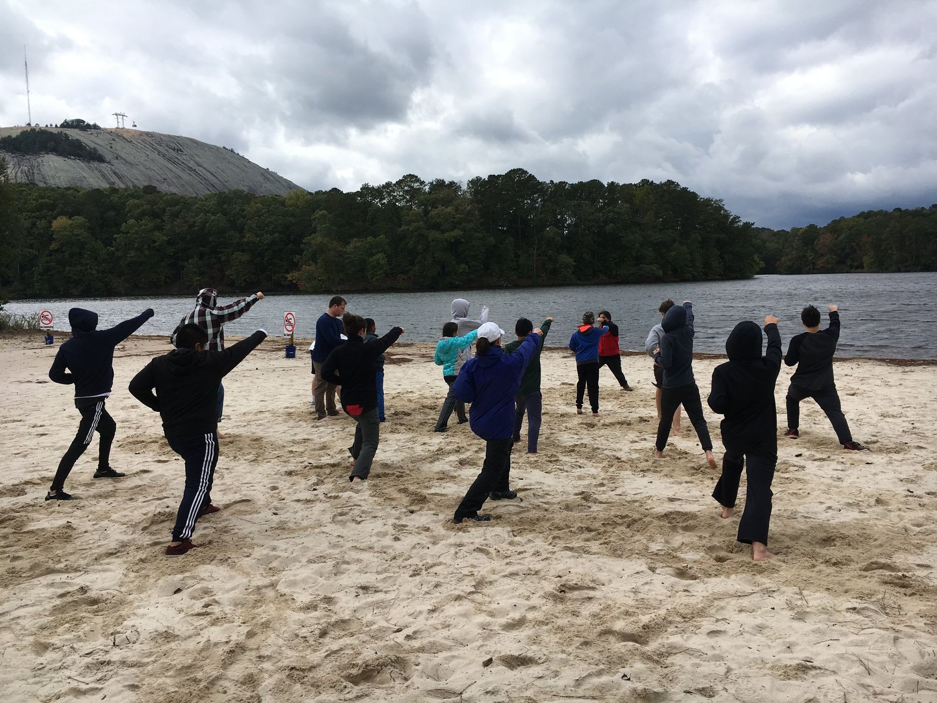 a group of people are standing on a sandy beach near a lake .