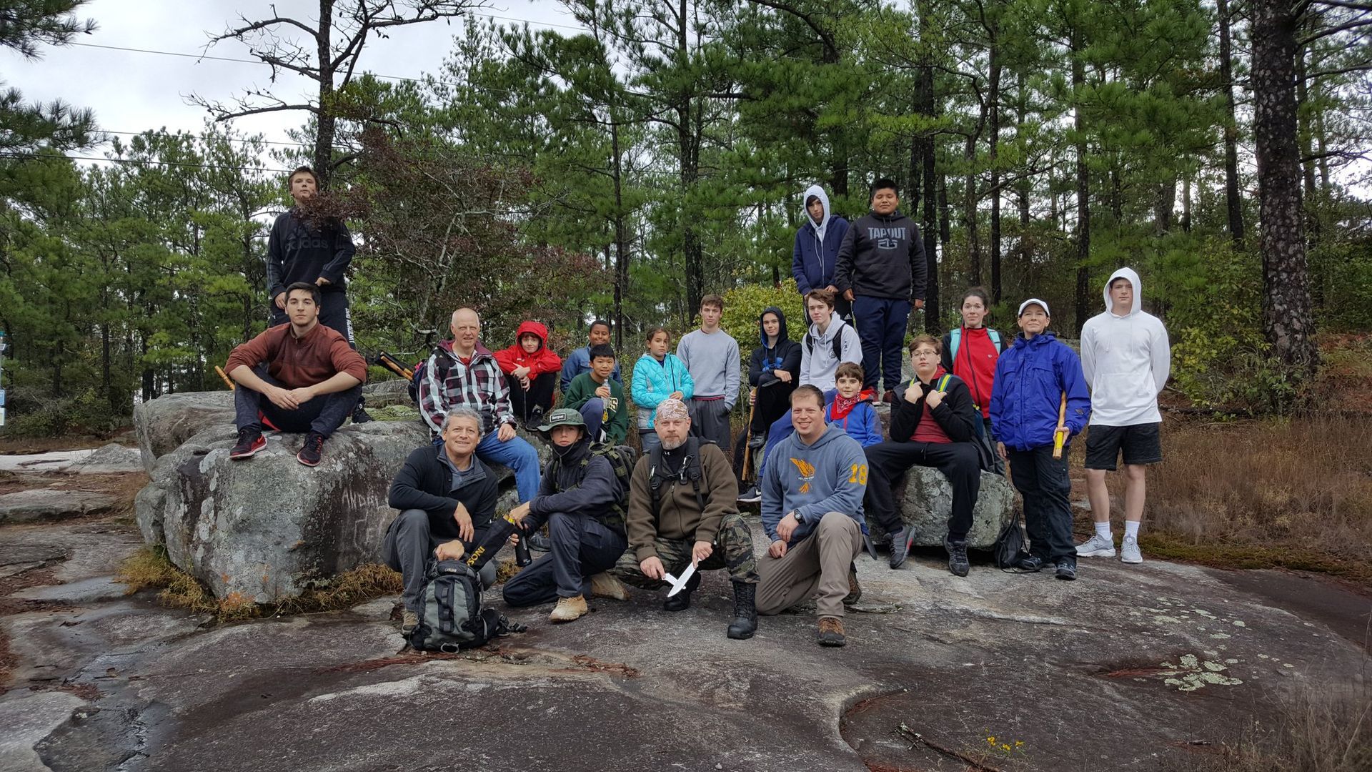 a group of people are posing for a picture on a rock in the woods .