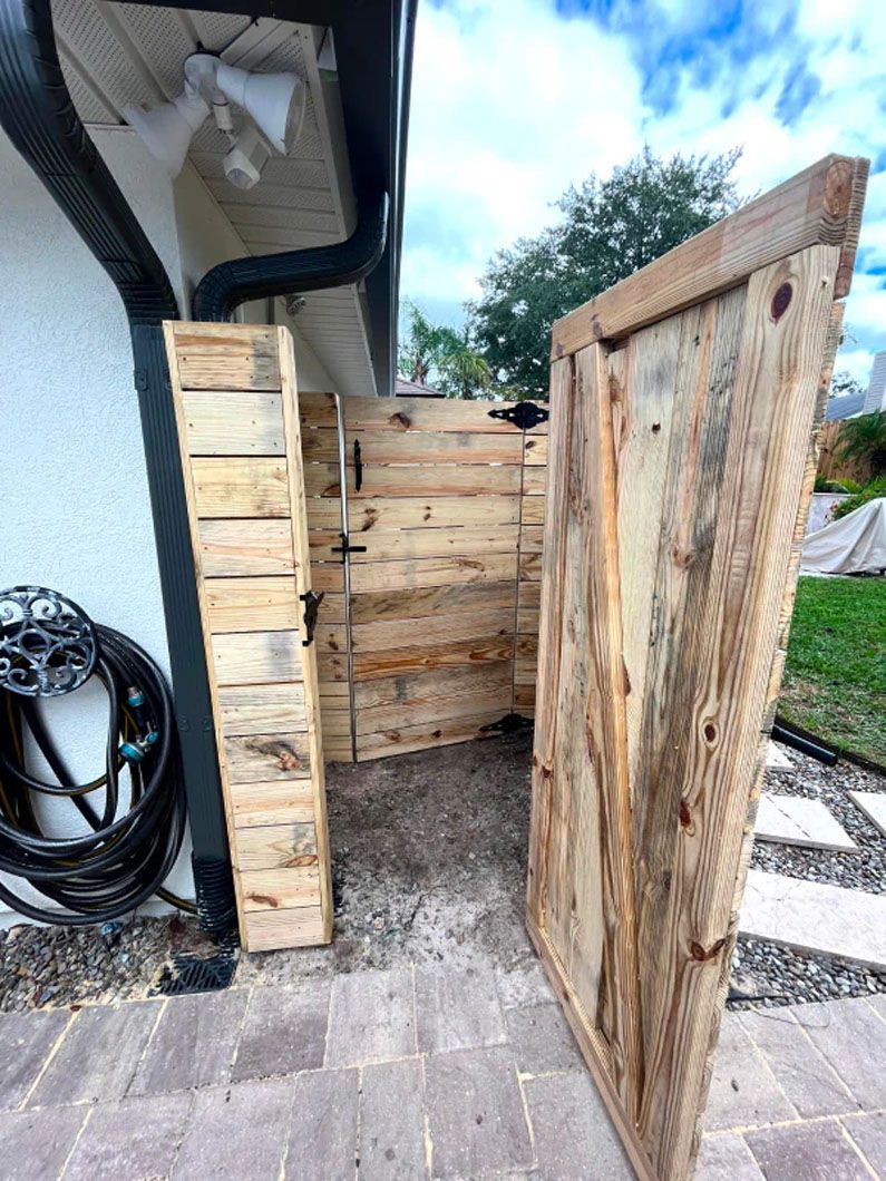 A wooden fence is sitting next to a house on a brick sidewalk.