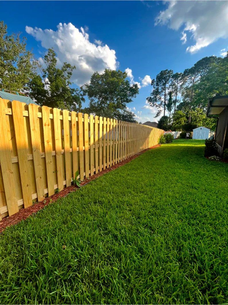 A wooden fence surrounds a lush green lawn in a backyard.
