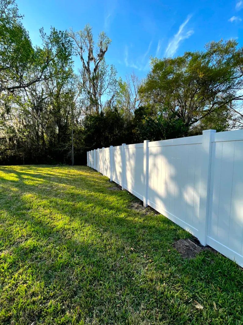 A white vinyl fence surrounds a lush green yard.