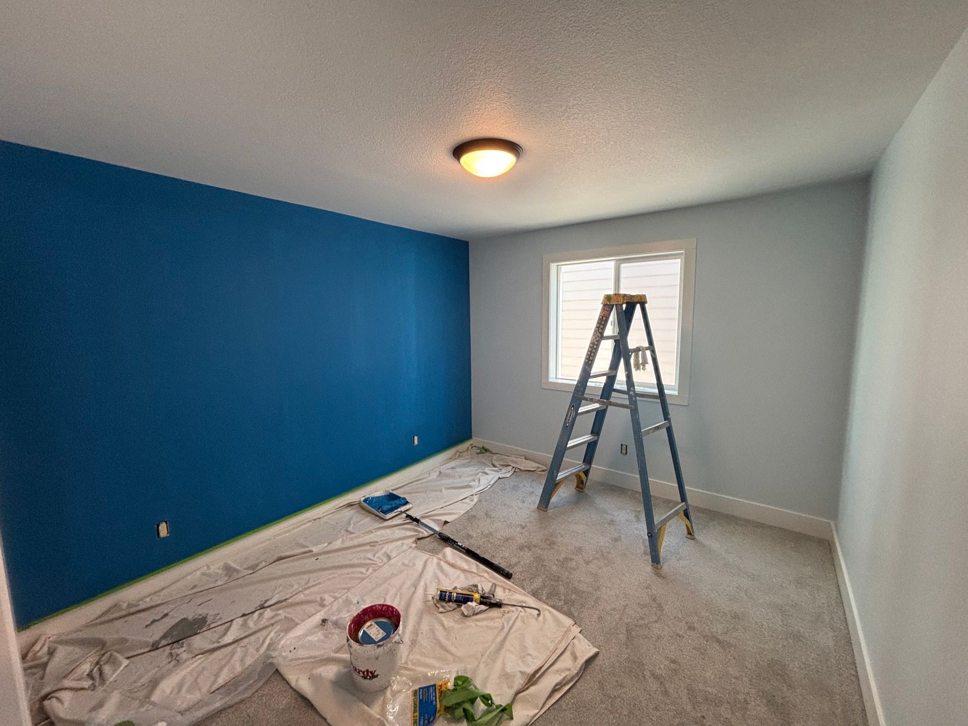 A room is being painted with blue walls and a ladder.