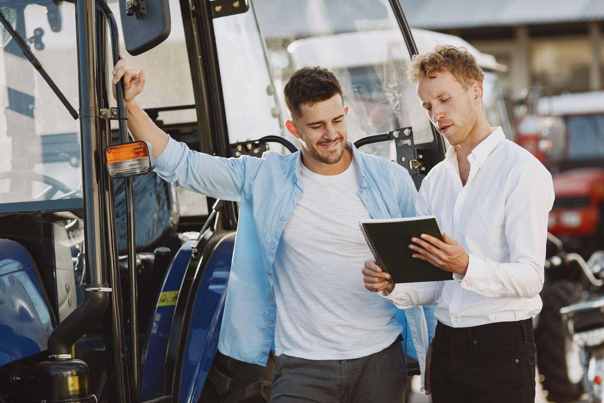 Two men are standing next to a tractor and looking at a tablet.