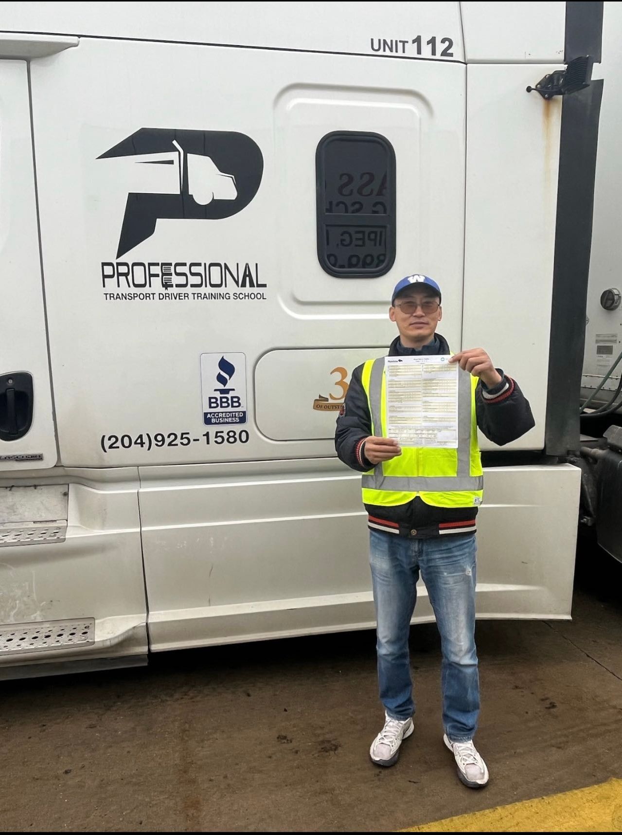 A man in a yellow vest is standing in front of a truck holding a certificate.