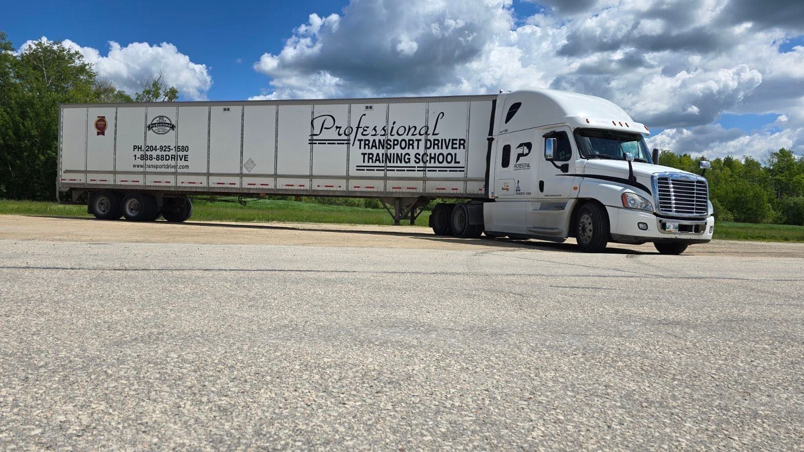 A white semi-truck with a Professional Transportation trailer parked on a gravel lot under a blue sky with clouds.