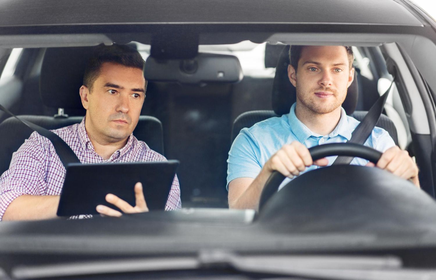 Two men are sitting in a car looking at a tablet.