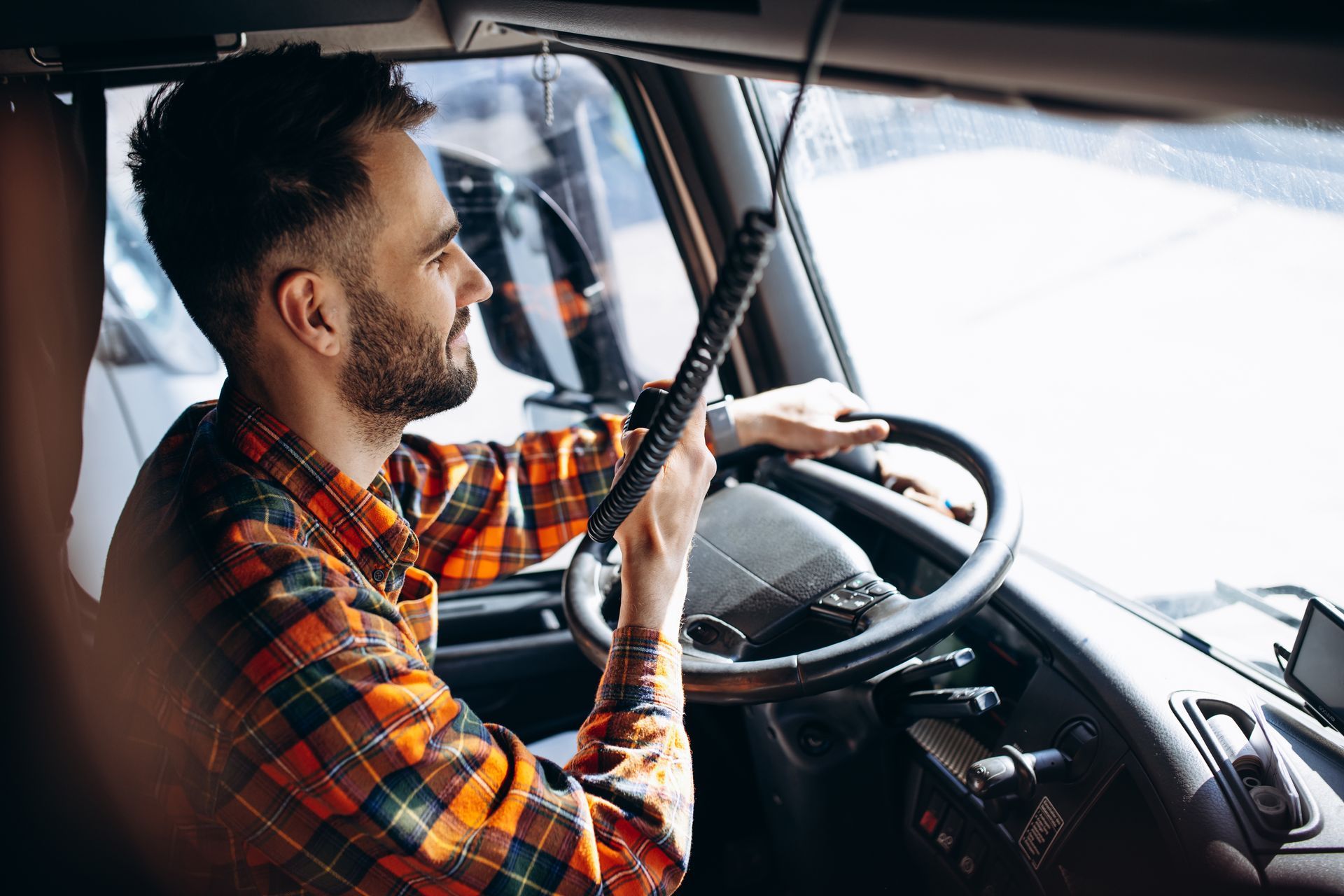 A man is driving a truck and talking on a walkie talkie.