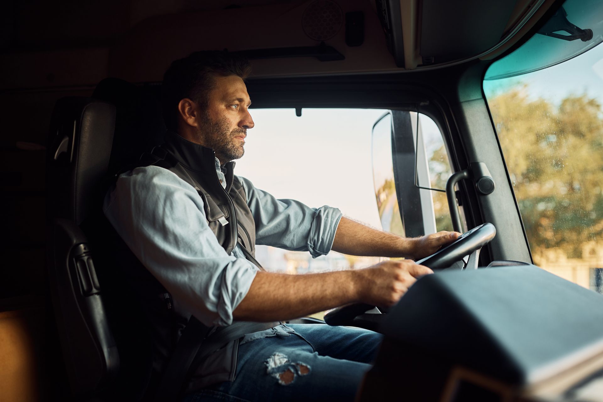Man driving a truck, holding steering wheel, looking forward, daytime setting.