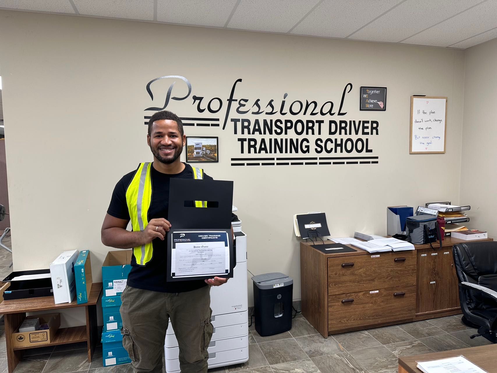 A man is holding a certificate in front of a wall that says professional transport driver training school.