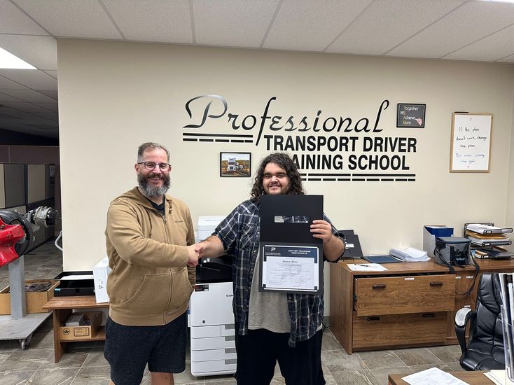 Two men shaking hands in front of a sign that says professional transport driver training school