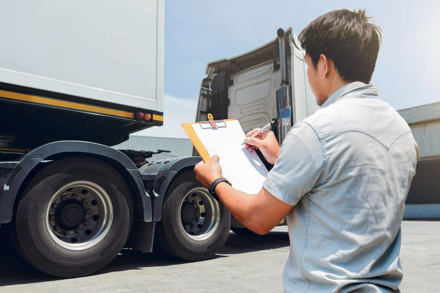 A man is writing on a clipboard in front of a truck.