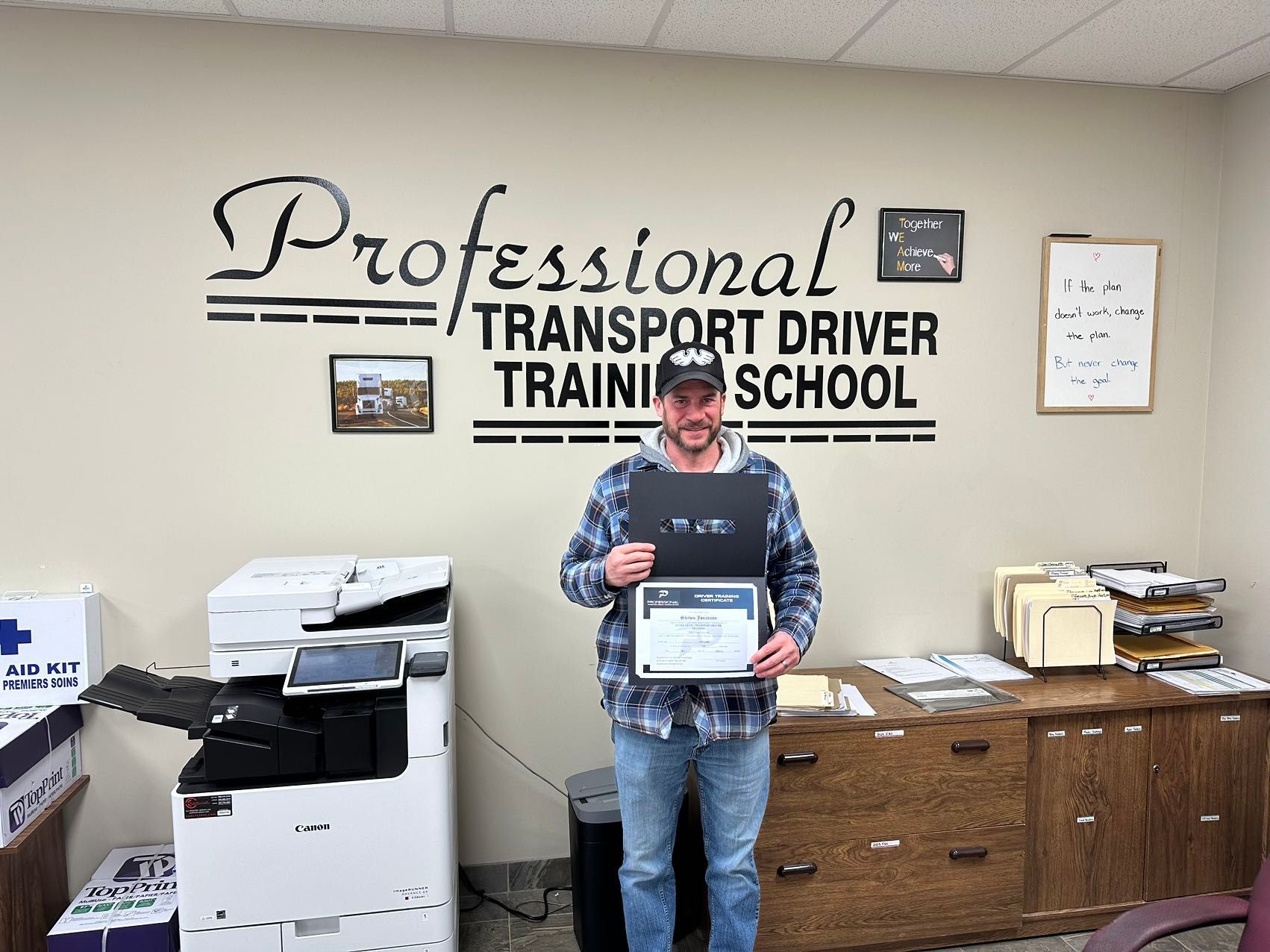 A man is holding a certificate in front of a sign that says professional transport driver training school