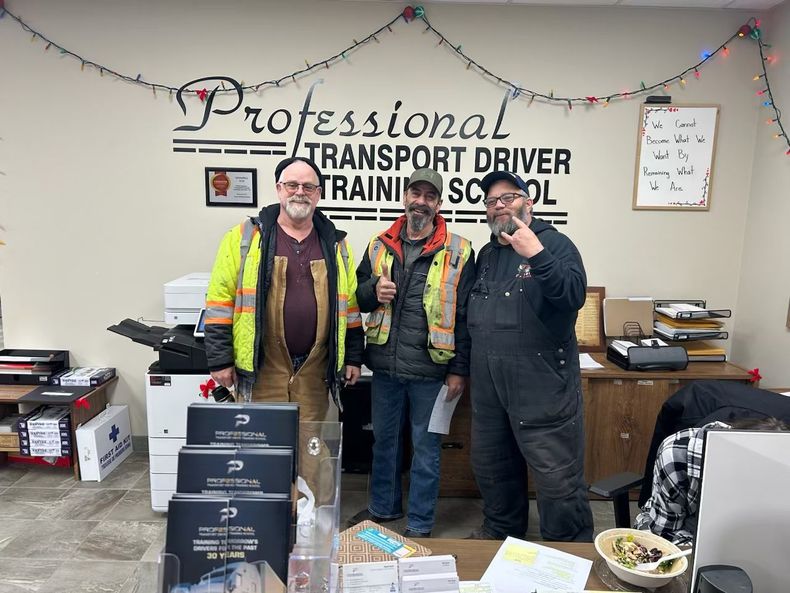 Three men are standing in front of a sign that says professional transport driver training school