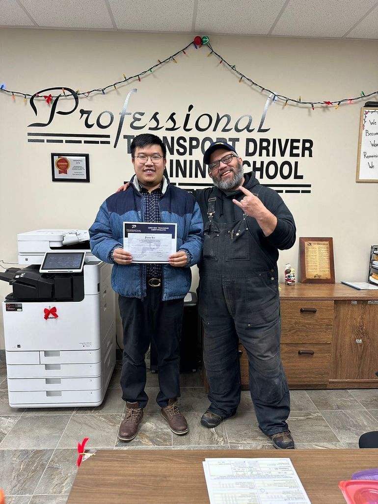 Two men are standing next to each other in front of a sign that says professional transport driver training school.