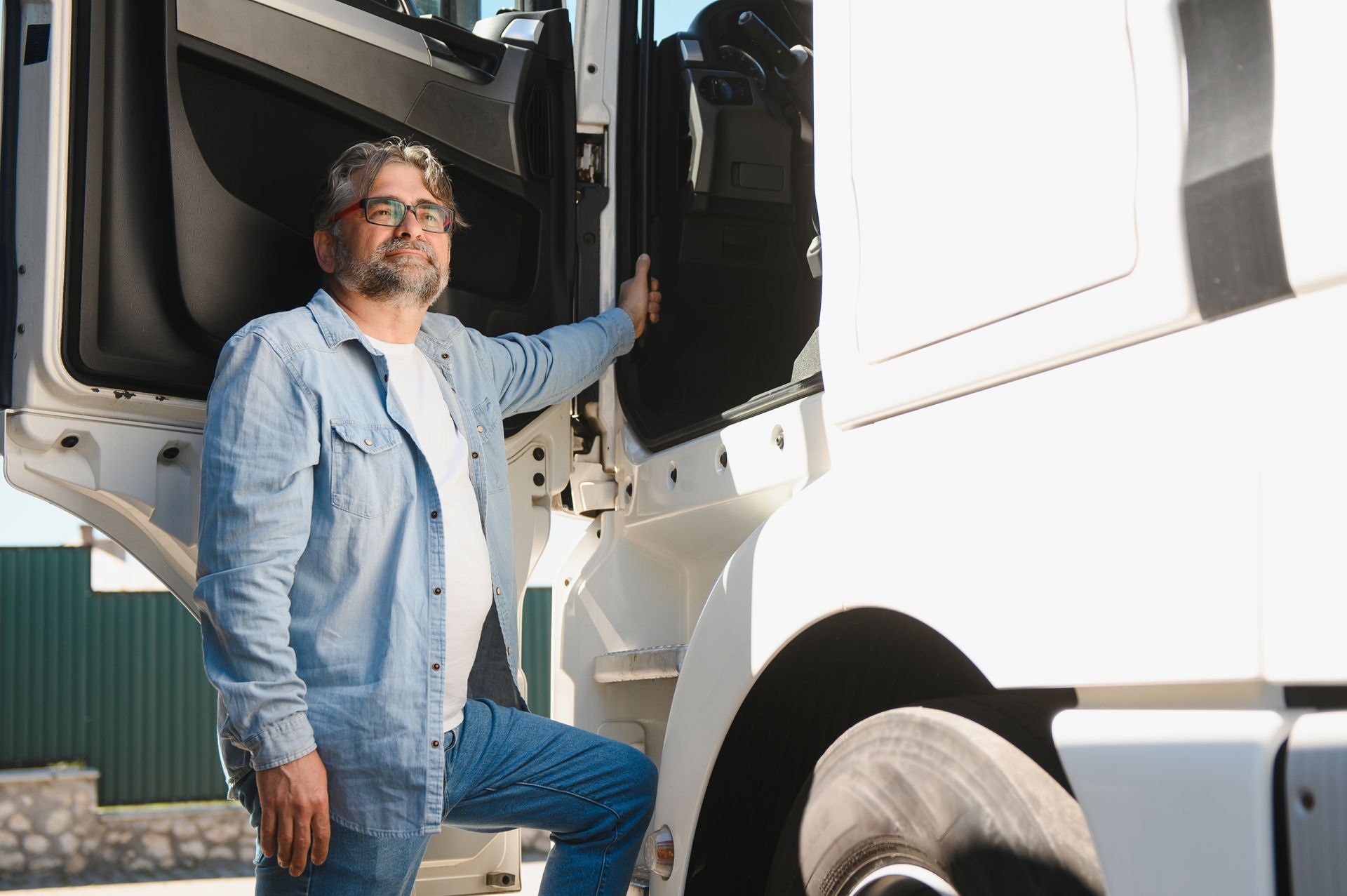 Man in blue shirt and jeans exiting a white truck, hand on door, smiling.