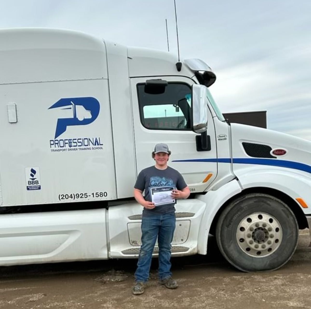 A person holding a document stands in front of a white Professional Transport semi-truck on a dirt lot.
