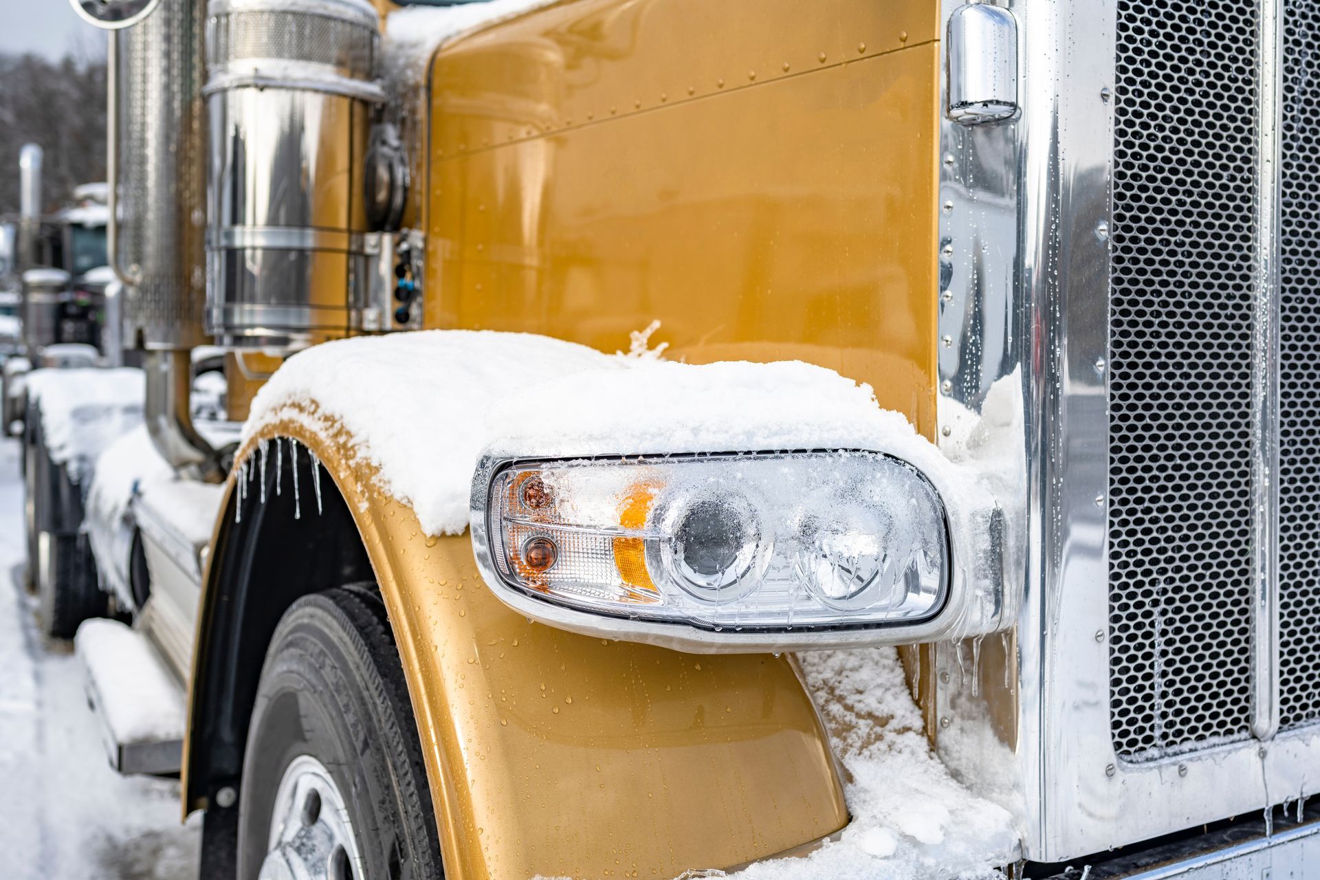 Gold semi-truck with snow-covered fender and headlight. Cold, winter setting.