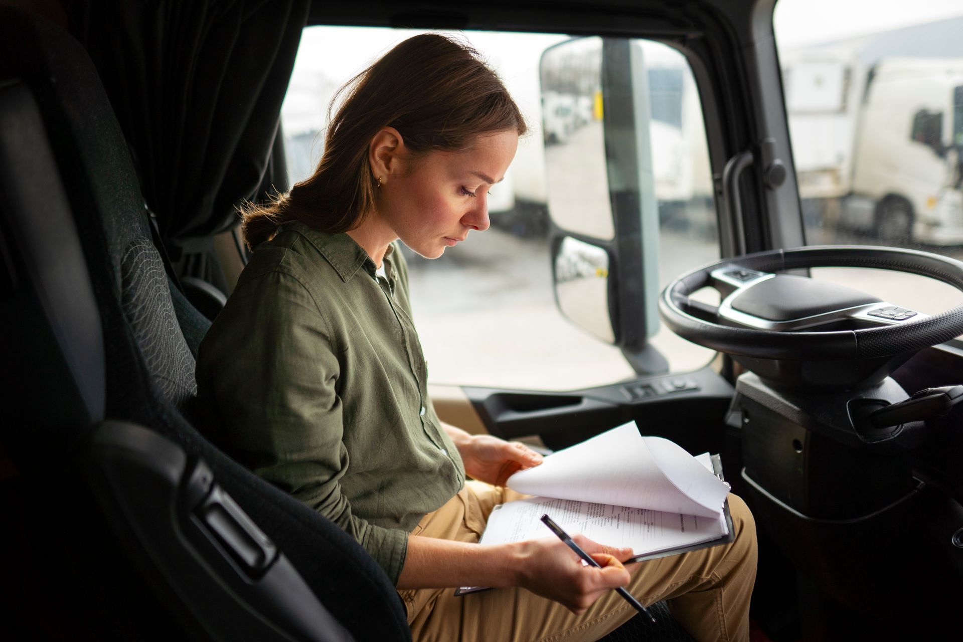 A woman is sitting in the driver 's seat of a truck writing on a clipboard.
