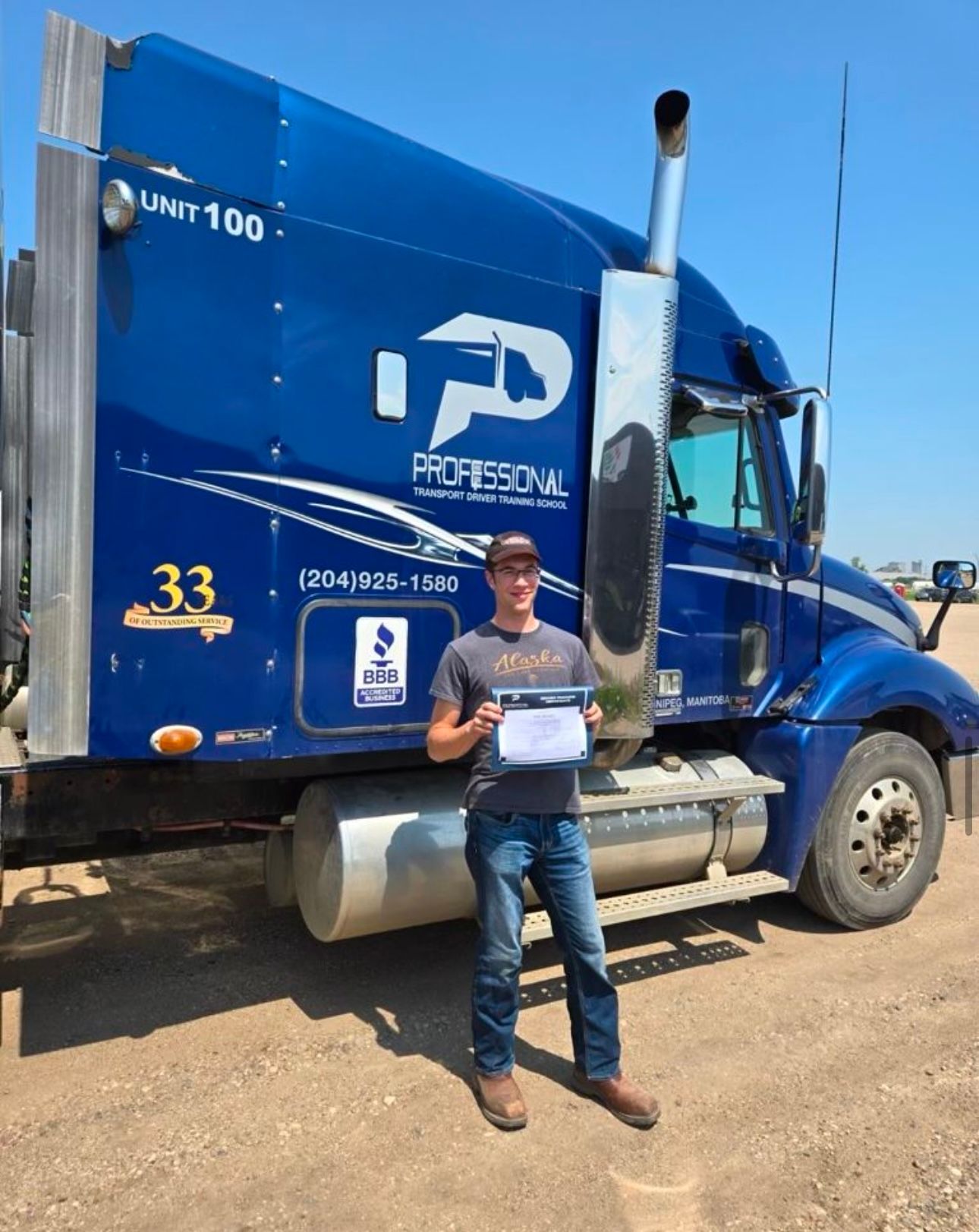 A man is standing in front of a blue semi truck holding a certificate.