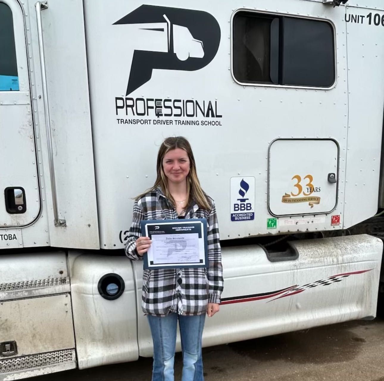 A person holding a certificate in front of a white truck for a professional transport driver training school.