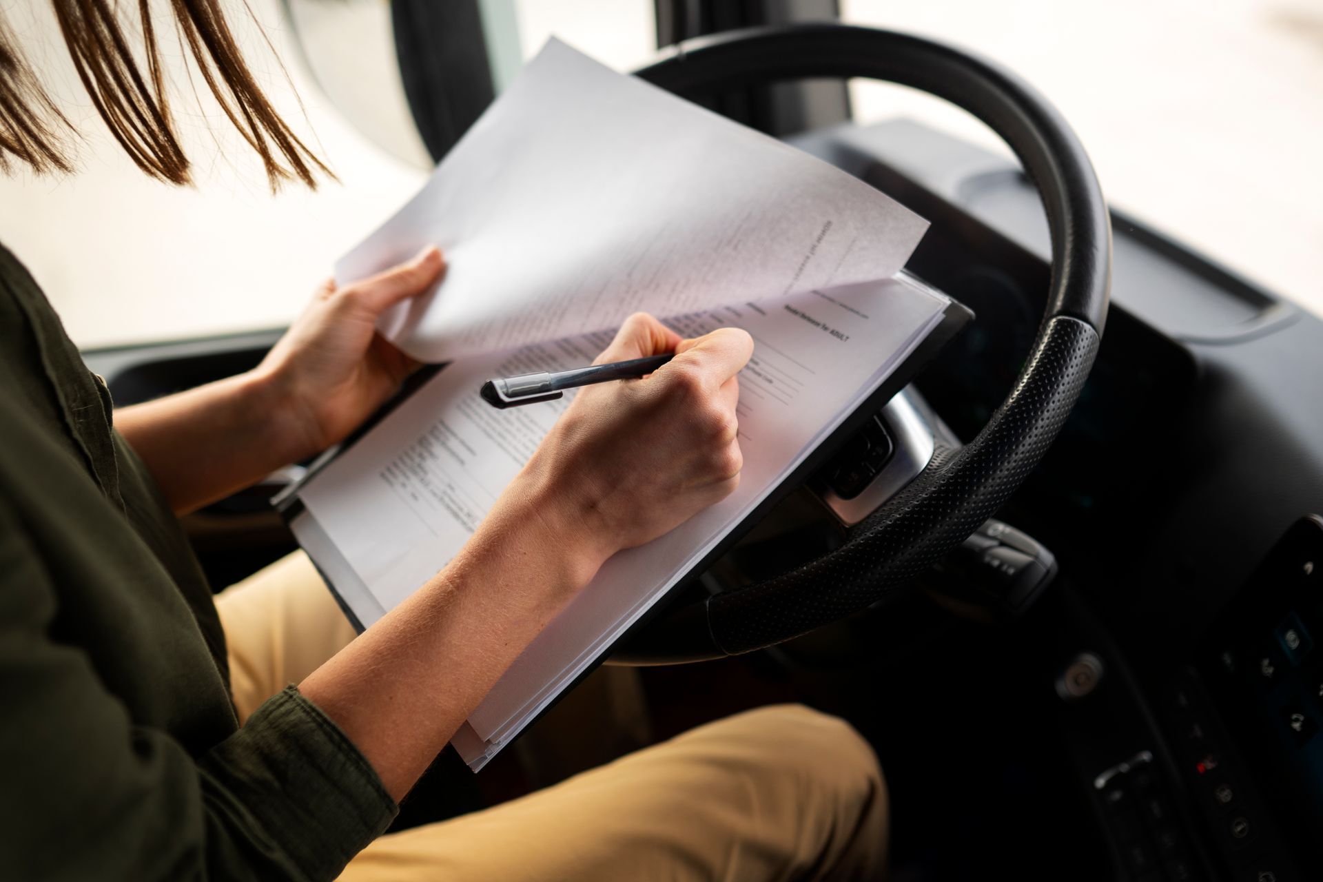 A woman is sitting in the driver 's seat of a truck writing on a piece of paper.