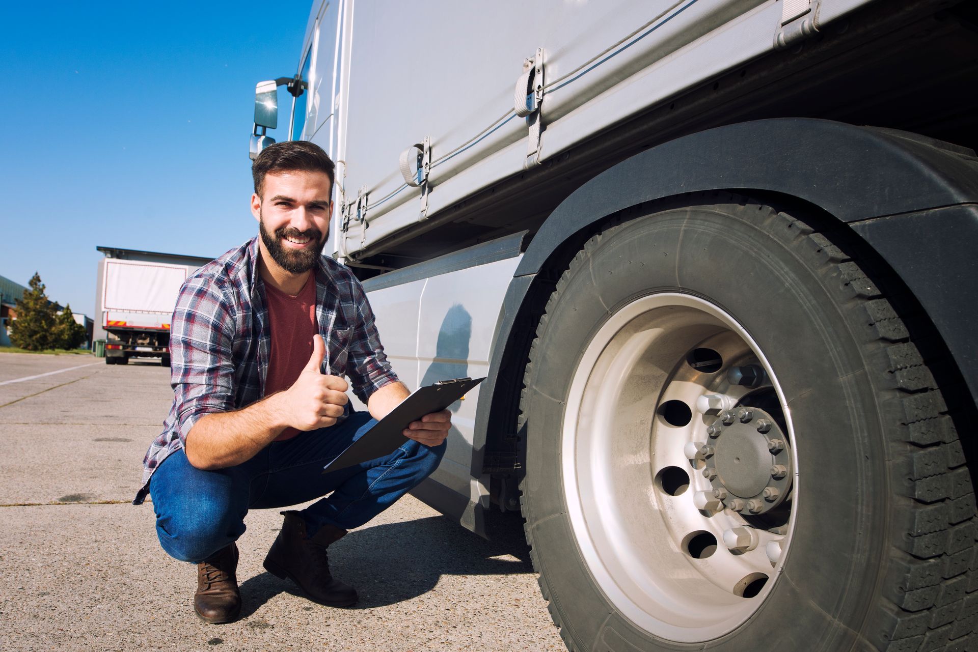 A man is kneeling down next to a truck holding a clipboard and giving a thumbs up.