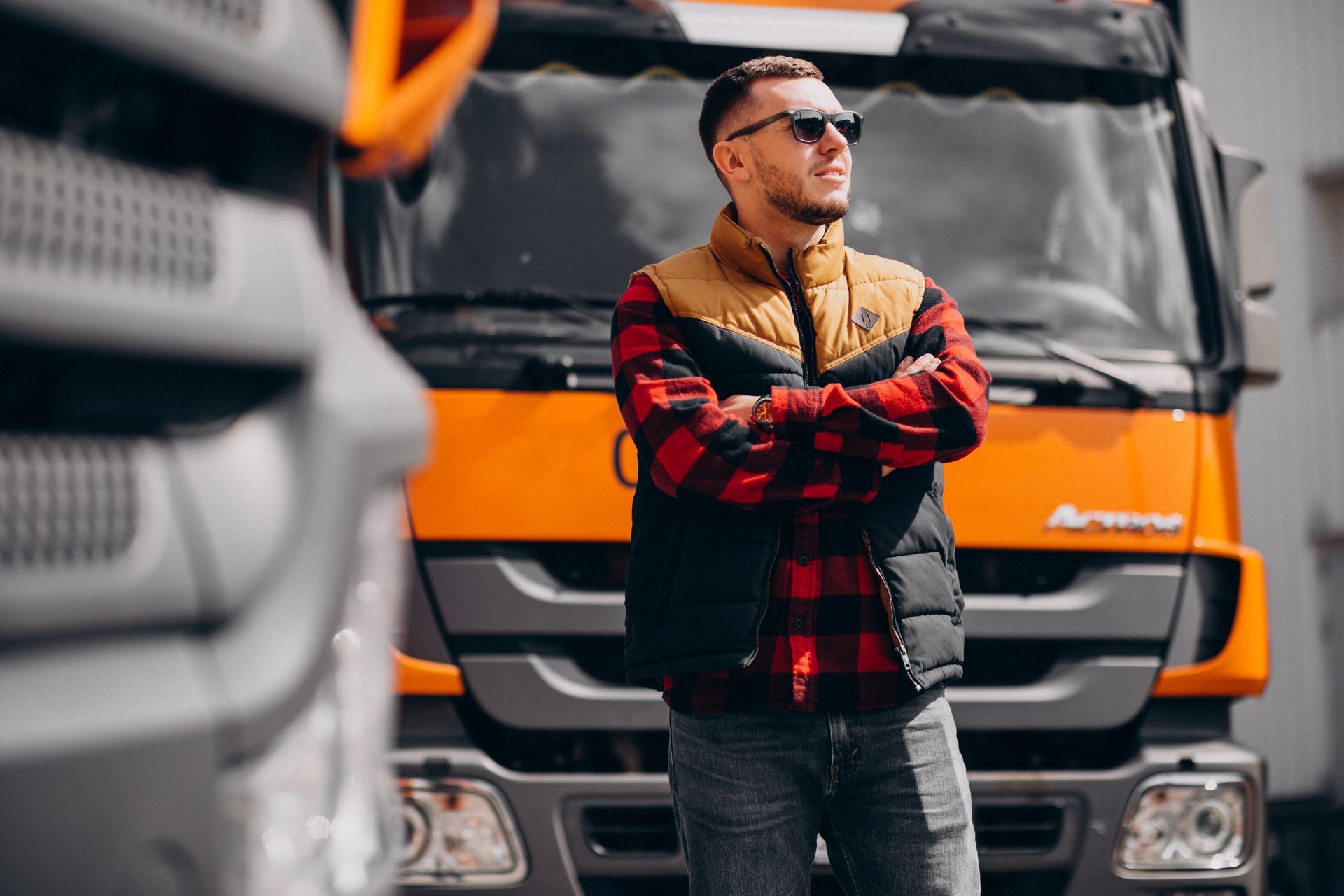Man in sunglasses and vest stands in front of orange truck.
