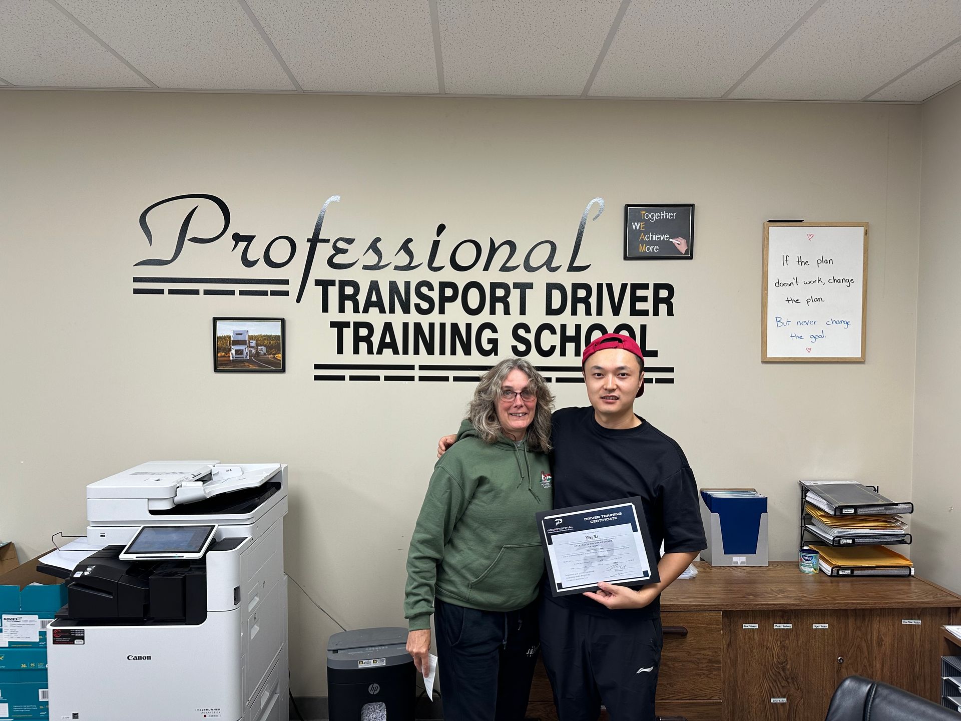 A man and a woman are standing in front of a sign that says professional transport driver training school
