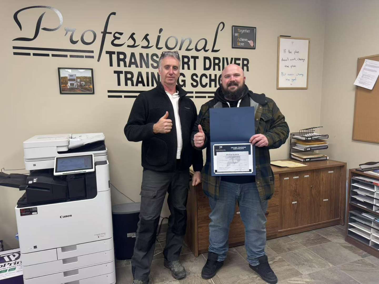 Two men are standing in front of a sign that says professional transport driver training school