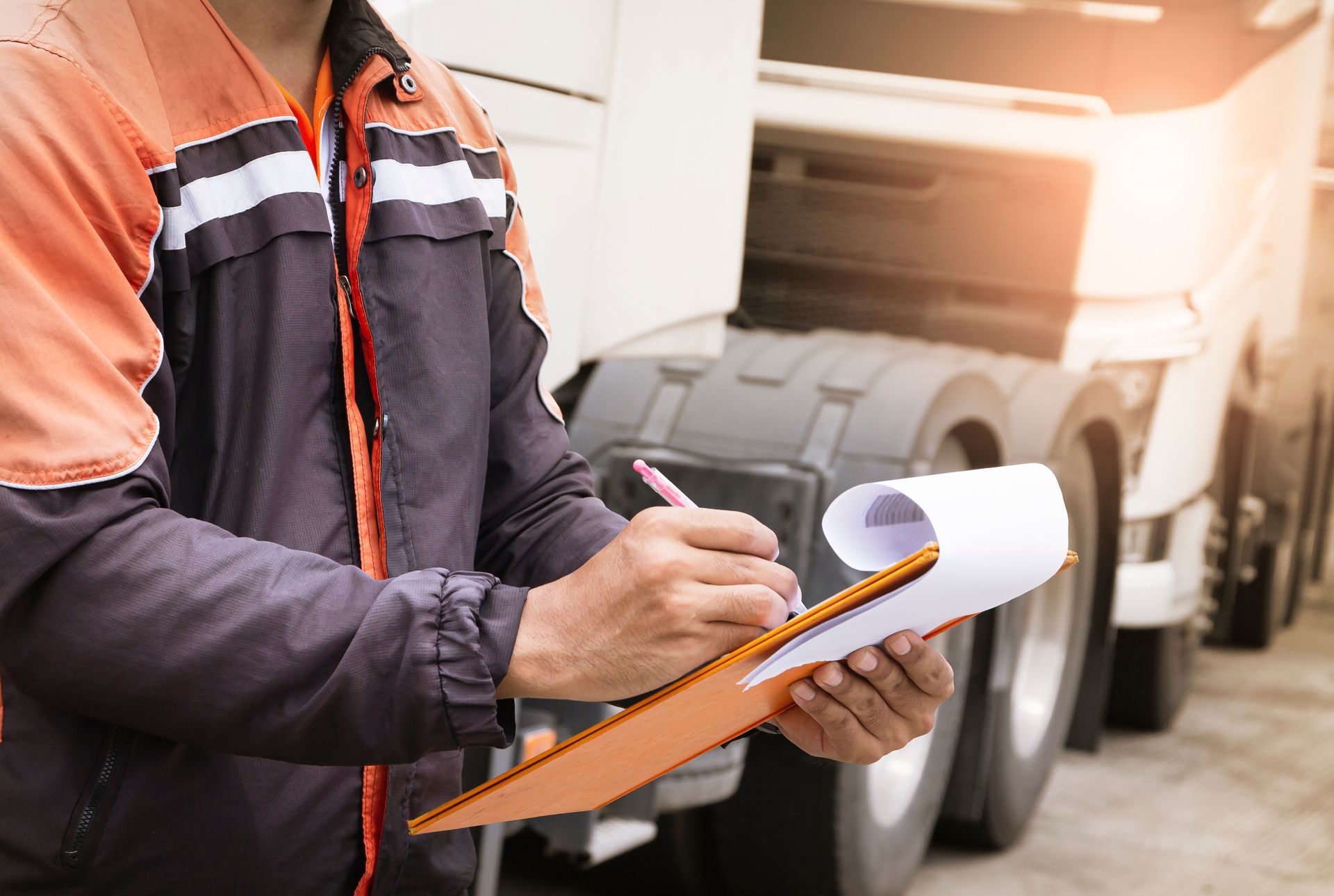 a man is writing on a clipboard in front of a truck .