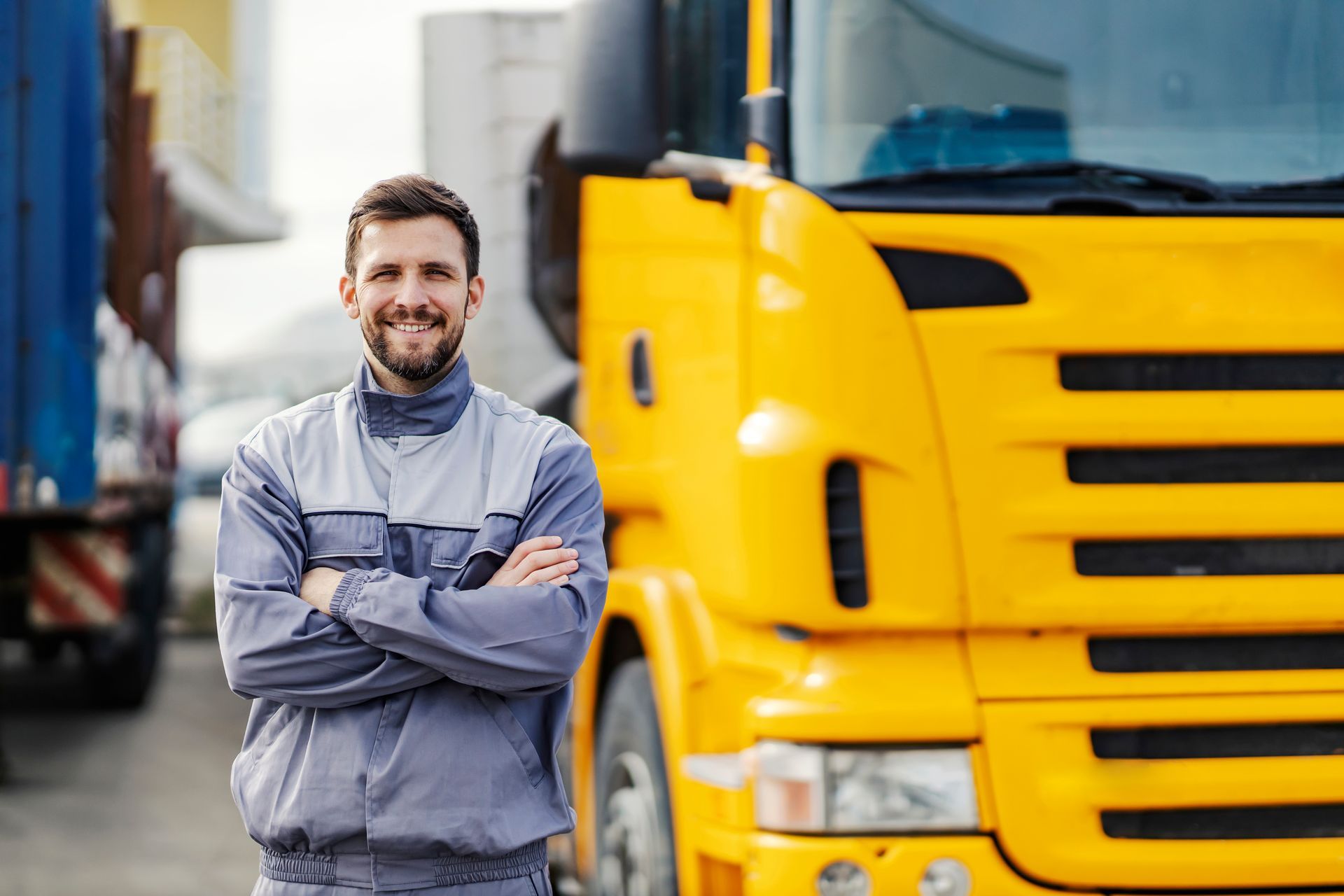 a man is standing in front of a yellow truck with his arms crossed .