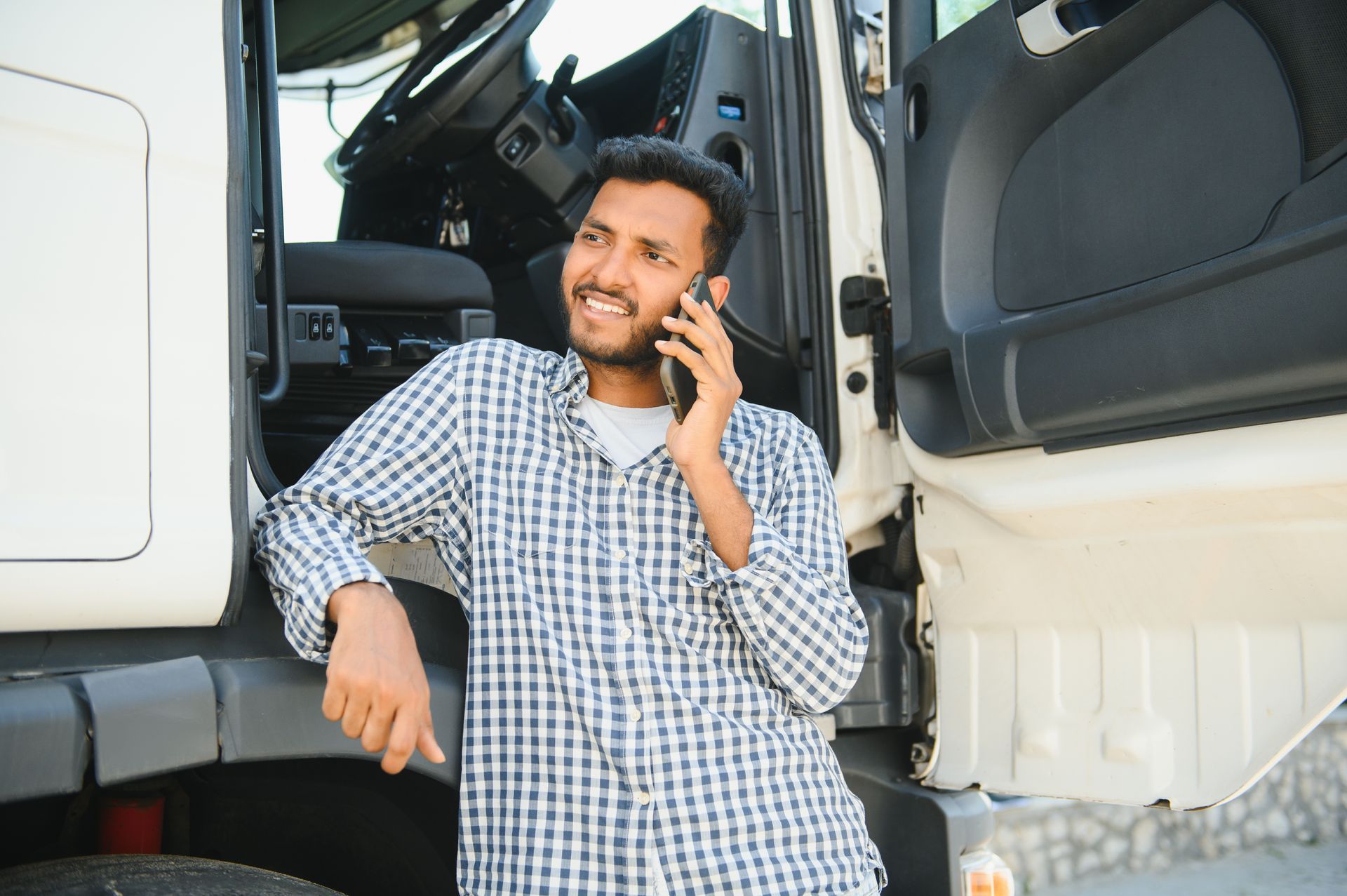 A man is leaning on a truck while talking on a cell phone.