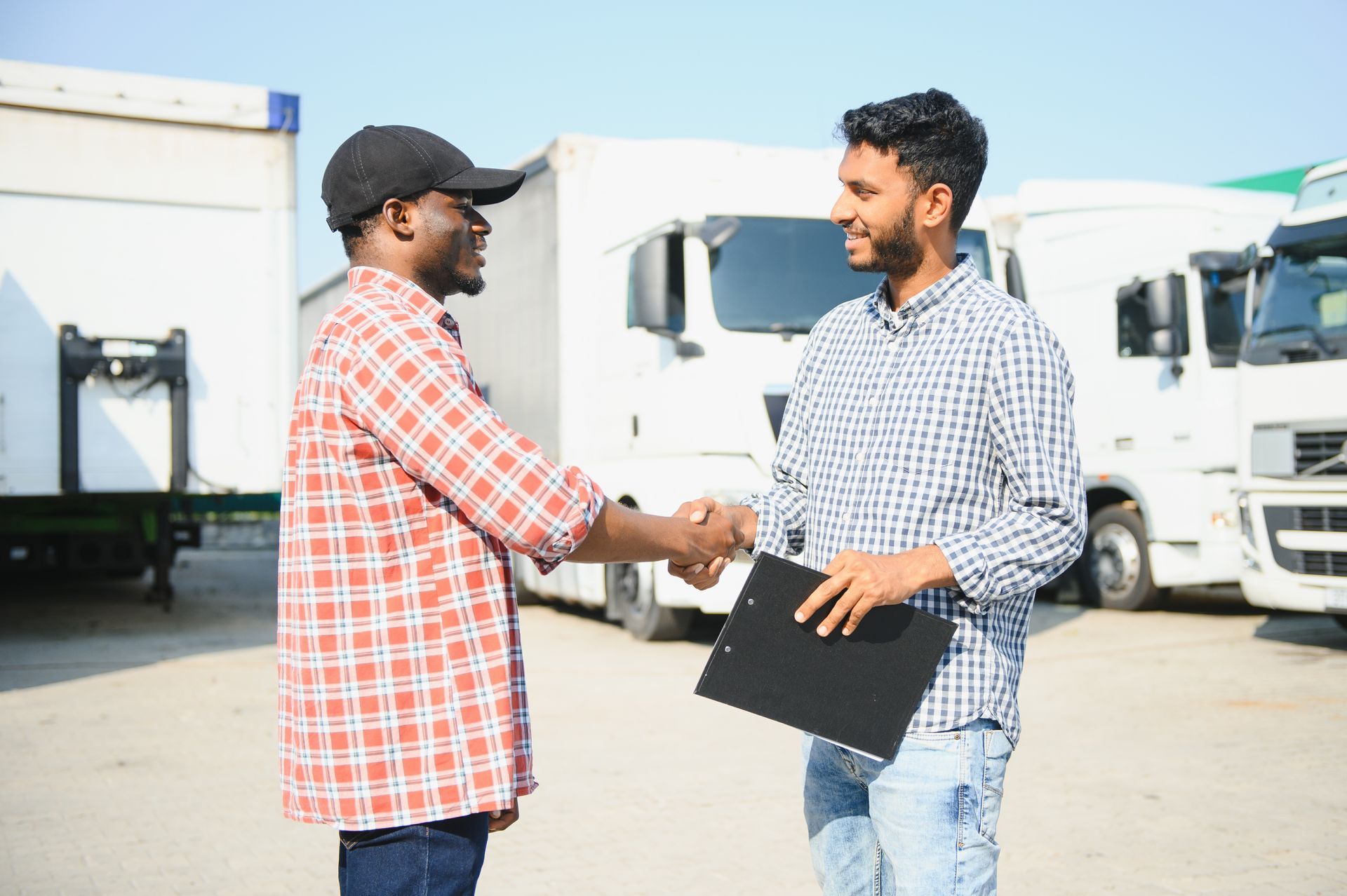 two men are shaking hands in front of trucks in a parking lot .