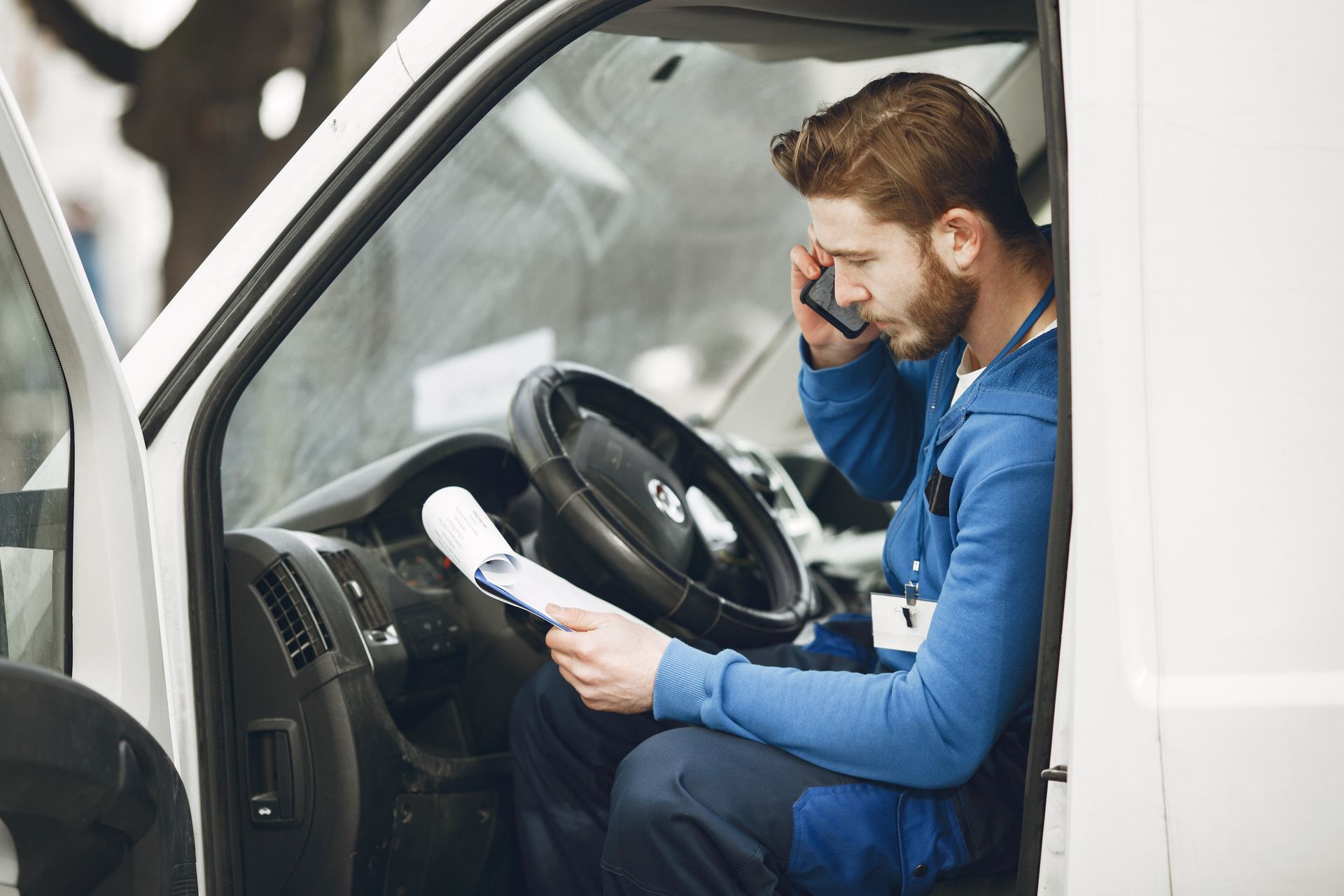 a man is sitting in the driver 's seat of a van talking on a cell phone .